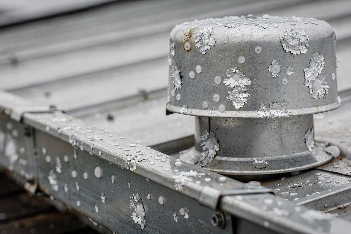 A galvanised roof vent cap and the metal edge below it, pitted with small round impact marks.